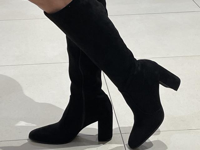 DeesseBleue's black thigh-high boots with chunky heels, standing on white tiled floor. Boots are slightly worn, showing subtle creases. DeesseBleue's shadow is visible on the floor.