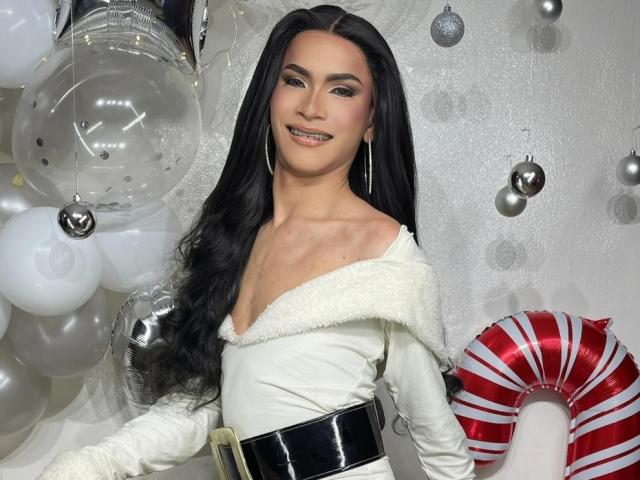 AgathaRodriguez has long black hair, a white off-shoulder top, black belt, and a smile. She's standing with white balloons, silver ornaments, and a red-striped candy cane.