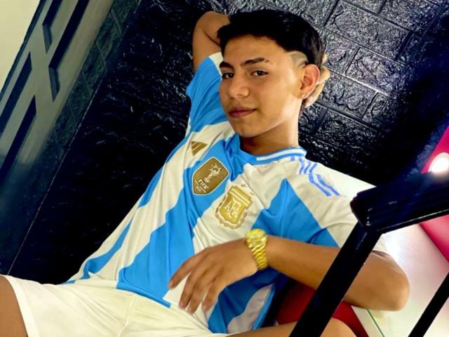 RichiiHott, with short black hair, wearing a blue and white soccer jersey, white shorts, and a gold watch, leaning back with a relaxed, slightly smug expression.