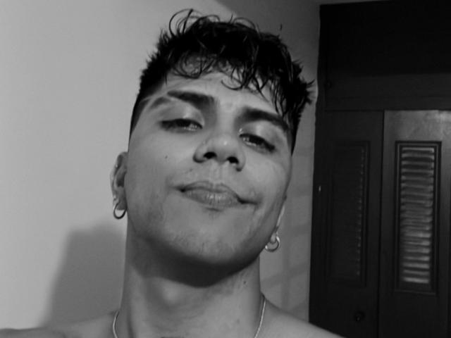 SebasAllen has short, curly black hair, a nose ring, and a hoop earring in his left ear, with a slight smile and a dirty face. Black and white photo.