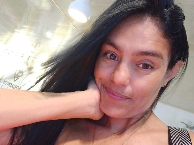 ElizabethManzon with long black hair, brown eyes, and a subtle smile, resting her chin on her hand, showing a gentle, cute expression and small, visible nipples.