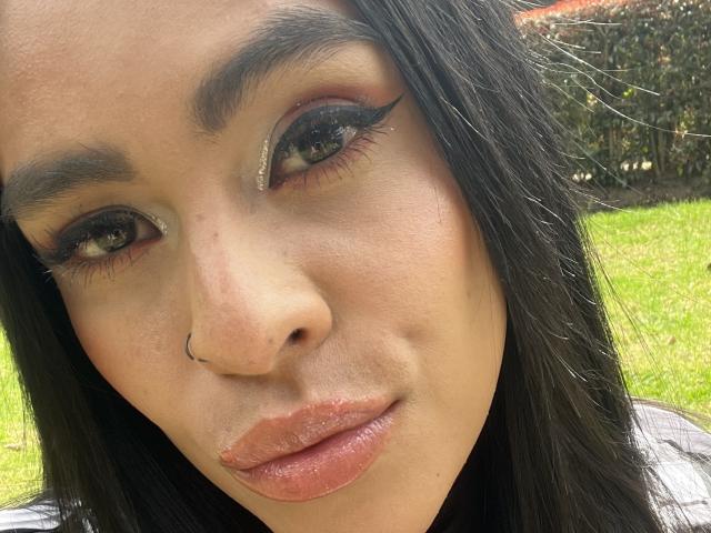StellaBeckker's face, showing full lips with a slight pout, black eyebrows, long eyelashes, and a nose ring, with dark hair and light brown skin, in a selfie.