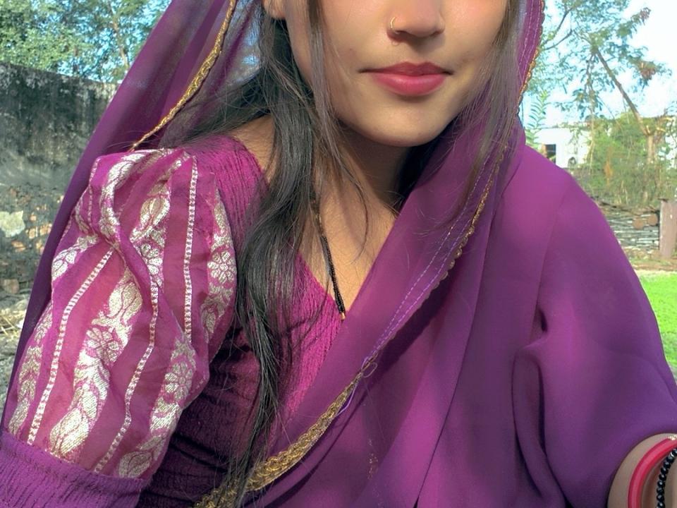 ivya999 con i capelli castani, indossa una maglia con un motivo viola e dorato e una sciarpa viola coordinata, mostrando il suo viso carino e le labbra rosa. Il seno è parzialmente visibile sotto la maglia..