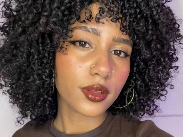 CinthiaWalker has curly black hair, brown eyes, and a nose ring. She's wearing glossy red lipstick and gold hoop earrings, with a slight pout on her shiny lips.