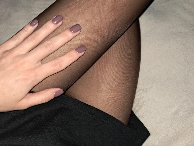 La mano di Amberia, con le unghie dipinte di viola, riposa sulla sua coscia, coperta da collant neri trasparenti. Si intravede l'orlo della sua gonna nera. Collant trasparenti, unghie viola, la coscia di Amberia..