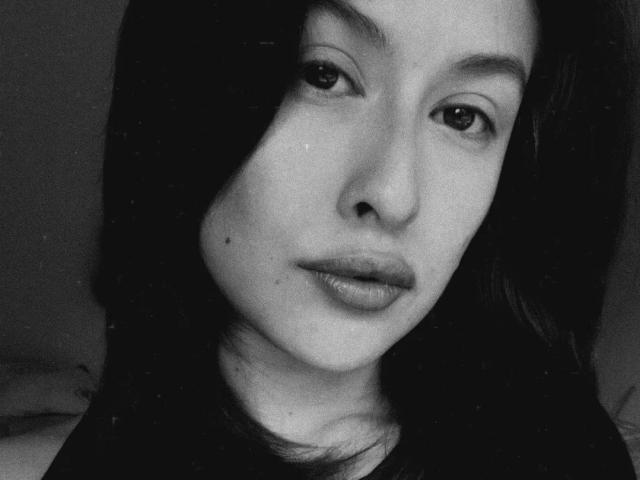 Black-and-white selfie of IsabellaPalacio with dark, wavy hair, slightly parted lips, and a small mole above her upper lip, staring directly at the camera.