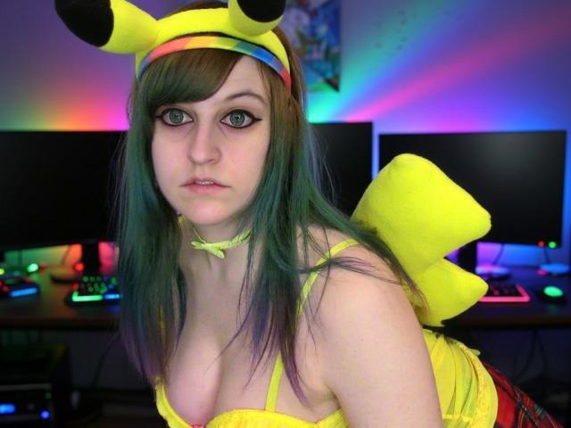 Zelda, com cabelo verde e roxo, vestindo uma fantasia de Pikachu com orelhas amarelas, uma faixa na cabeça e um laço, tem seios pequenos e uma expressão neutra em um quarto com iluminação colorida..