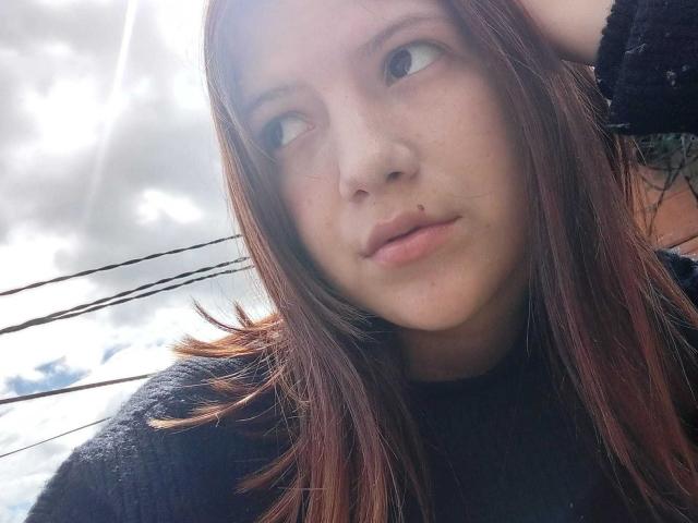 MiaBellee has light skin, brown eyes, and a nose piercing with a small ball. She's wearing a black sweater, with brown hair, and a slightly pouty expression.