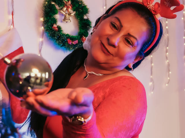MissLadyy with a red headband and reindeer ears, holding a shiny black ball, wearing a red lace top, smiling, and looking slightly to the side.