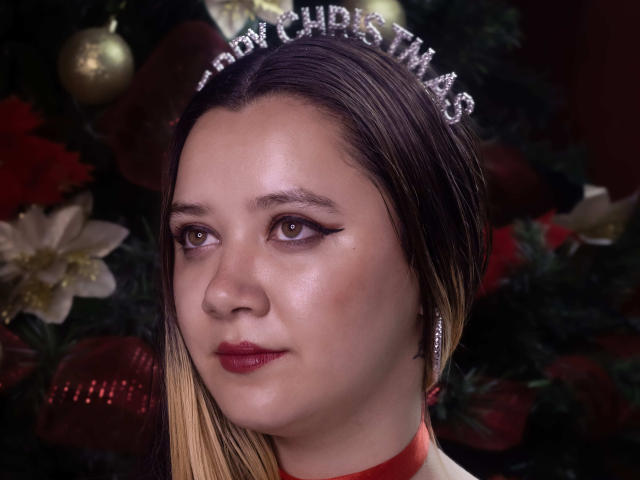 AlayaHot has a shiny face, dark brown eyes, red lipstick, and a glittery Christmas headband. Her blonde hair is slicked back, and she's wearing a red choker.
