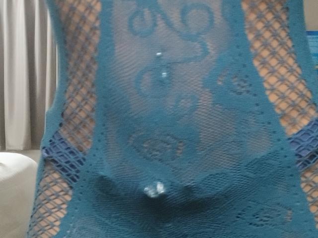 La robe bleu dentelle de Prettycat88i, qui révèle ses seins et ses parties intimes à travers le tissu, avec un piercing visible au nombril et ses mamelons légèrement visibles à travers le tissu..