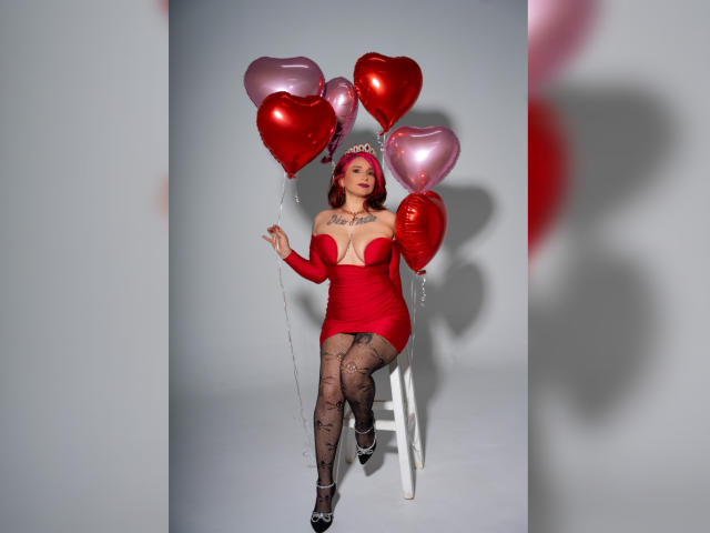 Alexandrapsique, red dress, heart-shaped balloons, standing on white stool, black fishnet stockings, red headband, silver heels, tattoos on chest, holding balloons, red and pink balloons.
