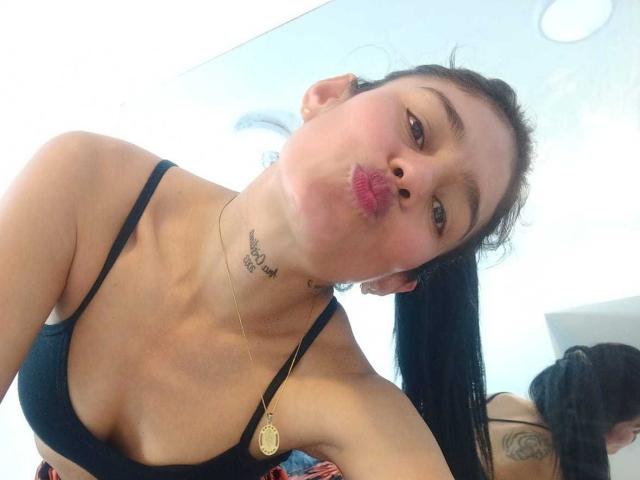 ElizabethManzon with black bra, pouty lips, and a necklace, showing her small tits and tattooed neck in a mirror selfie. She has a ponytail and a cute face.