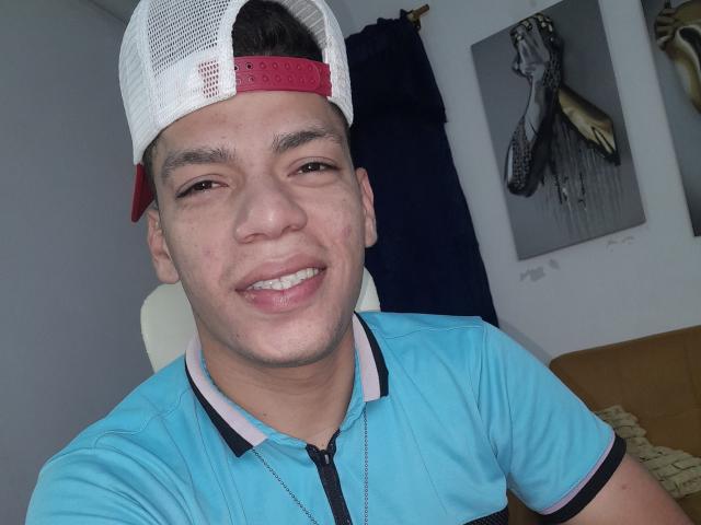 Andressant, a young dude with a light skin tone, short brown hair, and a white/red cap, smiling with his tongue slightly out, wearing a blue polo shirt.