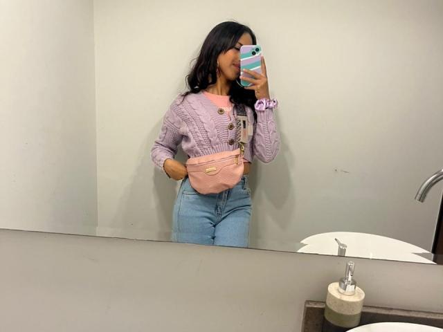 MyaaTyler with long black hair, pink sweater, and blue jeans, showing a small pink purse, taking a mirror selfie in a bathroom, her ass is slightly visible.