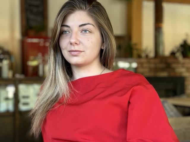 EmilyWilsonsy with blonde hair, blue eyes, red shirt, slight smile, subtle freckles, medium tits, slight blush, indoors, casual.