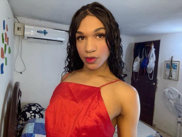 KendallKiss with curly black hair, wearing a red satin spaghetti strap dress, showing small tits and a cute face, standing in a room with a fan and air conditioner.