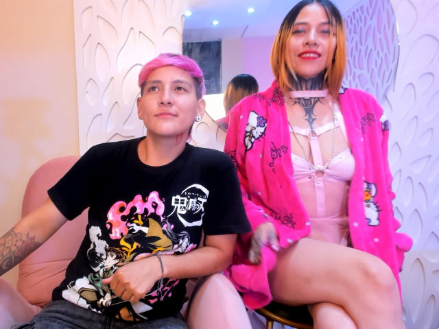 HadeDanny with pink hair and black shirt sits next to HadeDanny with orange-brown hair, pink robe, and white lingerie, showing tattoos and a chest necklace.