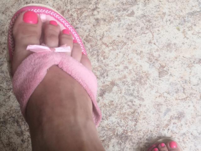 ItsMarry's foot with pink toenails, wearing a pink flip-flop with a small bow, on a textured, patterned surface. The flip-flop covers the toes, showing the pink bow.