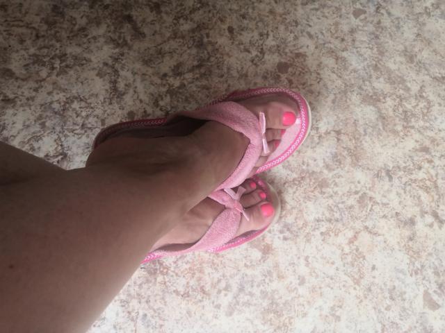 ItsMarry's pink sandal-clad foot with neon pink toenails, crossed at the ankle, on a speckled floor.
