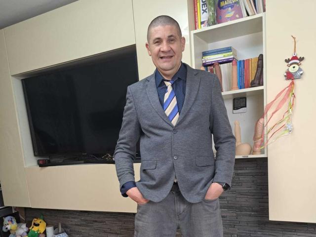 CrisSalon is a middle-aged dude with a shaved head, wearing a grey suit, blue shirt, and striped tie, standing with hands in pockets, smiling.