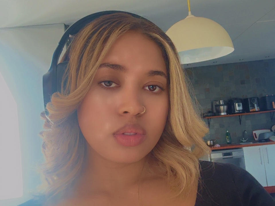 MissMidnight has light brown skin, wavy blonde hair, a nose ring, and is wearing black headphones. Her pouty pink lips are slightly parted. She's in a softly lit room.