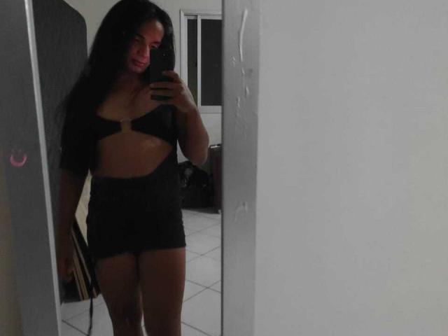 Aripietra with long black hair, wearing a black cutout top and shorts, showing her small tits and slim ass, taking a mirror selfie with a phone.