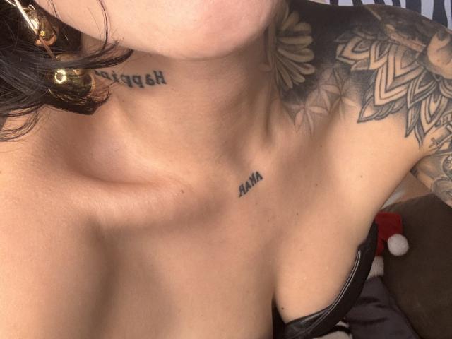 HannaBorbon's neck with tattoos, showing a small black tattoo below the jawline and a large floral tattoo on the right side. Her chest with cleavage, wearing a black strap.
