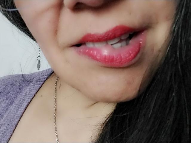 LailaCastillo's shiny pink lips are slightly open, showing a hint of teeth. She's wearing a purple top and a silver chain necklace, with black hair on the right.