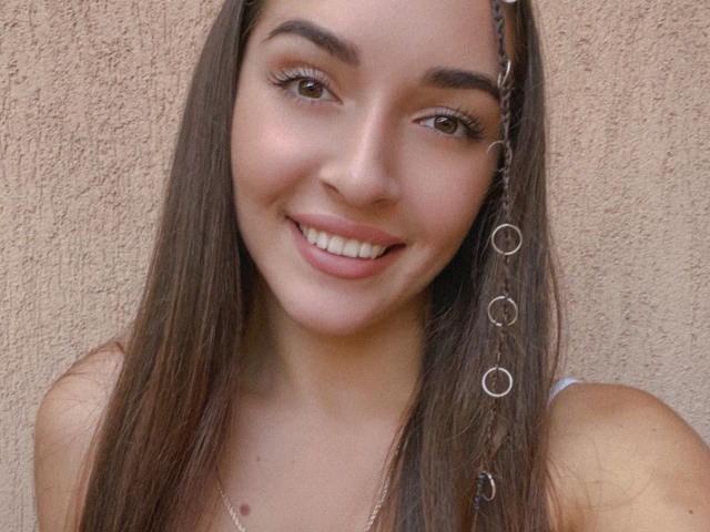 AquaLady with long brown hair, smiling, wearing a chain with circles on her right side, has brown eyes, and is looking at the camera, showing her white teeth.