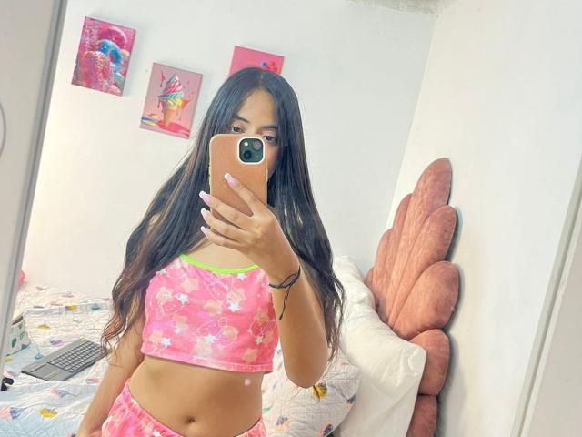 TamaraPeach with long brown hair, wearing a pink floral crop top and matching shorts, taking a mirror selfie with a pink phone, showing her flat stomach and small ass.