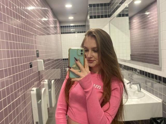 PamelaXu with long brown hair, pink ribbed sweater, and pale skin, taking a mirror selfie in a bathroom, holding a green phone, showing her tits.