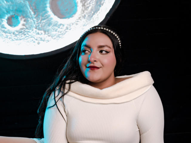 VictoriaRiver with long black hair, pearl headband, white ribbed sweater, and subtle smile, blue light on left side of face, dark background, slightly chubby, confident.
