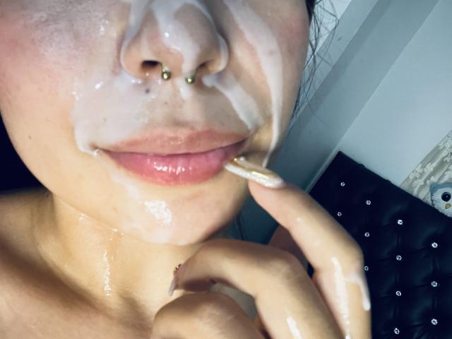 EileenSwift's face, covered in creamy white fluid, with a nose piercing, slightly parted pink lips, and her finger touching her lip. Her skin is glistening.