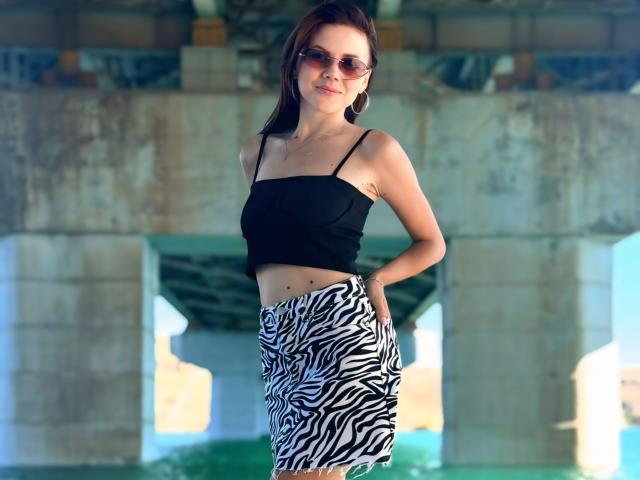 SexyVictoriaLove with small tits, wearing a black strap top and zebra-striped skirt, standing under a bridge, hands in pockets, smiling, wearing sunglasses, brown hair, casual, cute.