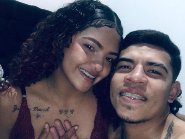 DirtyCoupleXy woman with curly brown hair, medium tits, and a tattoo on her chest, smiling. DirtyCoupleXy man with short black hair, small goatee, and teeth gap, smiling.