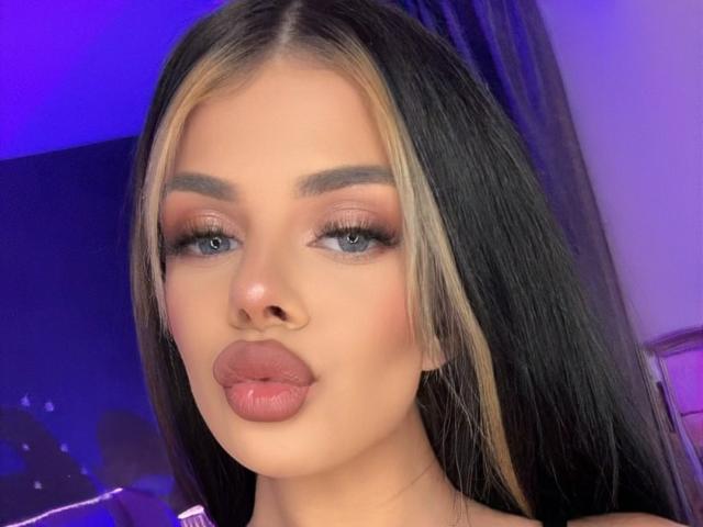 IvyRaven has long black and blonde hair, full pink lips, and blue eyes with dark eyeliner and pink eyeshadow. Her eyebrows are thick and she's looking directly at the camera.