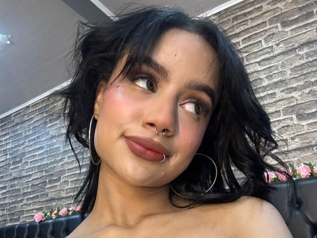 WendyJames has dark, wavy hair, a nose ring, and hoop earrings. She's looking sideways with pink lipstick and a slight smile, showing her cute ass.