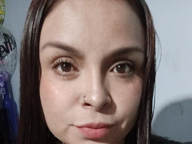 EntoncesIrene has light skin, brown eyes, and straight brown hair. She's pouting with a small nose ring on her left side. Her lips are slightly pink.