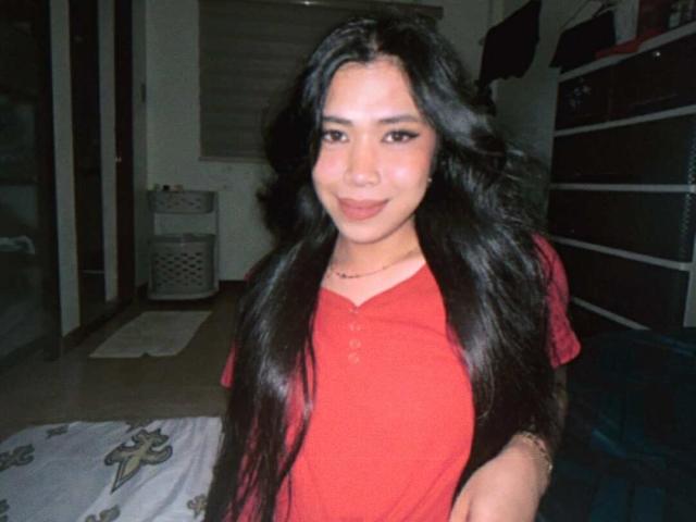 MsAnastasia has long black hair, wearing a red shirt, smiling with slightly parted lips, showing her small nose ring and a subtle tan. Her tits are not visible.