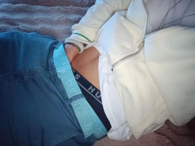 19yayo88-hot's hand is in their blue pants, revealing a black HUGO underwear with a visible white waistband. They're wearing a white, zip-up jacket.