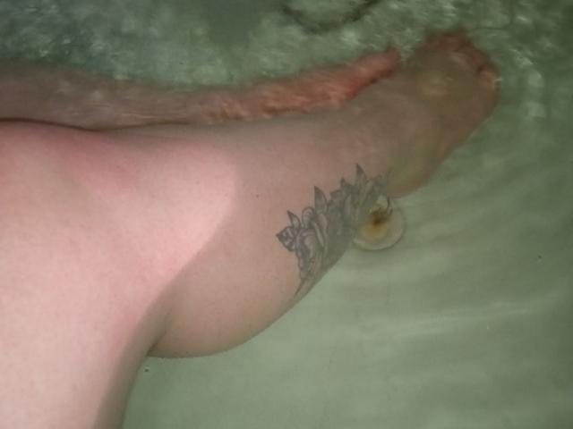 MyraKeldy's ass, tattooed leg, and foot in a bathtub with water, showing a detailed black and gray flower tattoo on her right calf. Her toes are visible.
