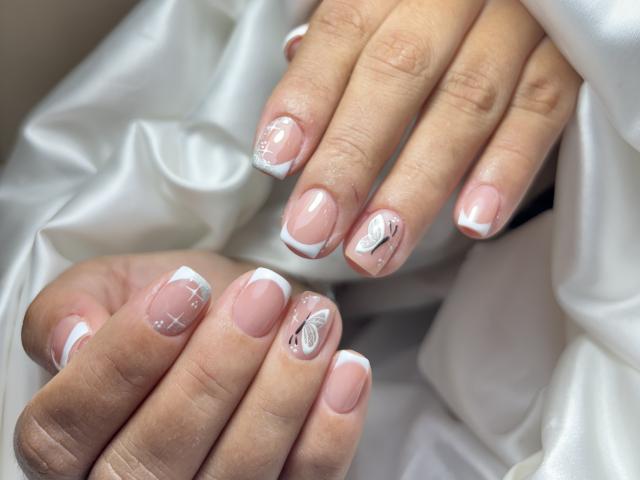 CristalWil's hands, showing off pink-nail manicure with white French tips, and small white designs like X's and a heart on her nails, resting on white satin.