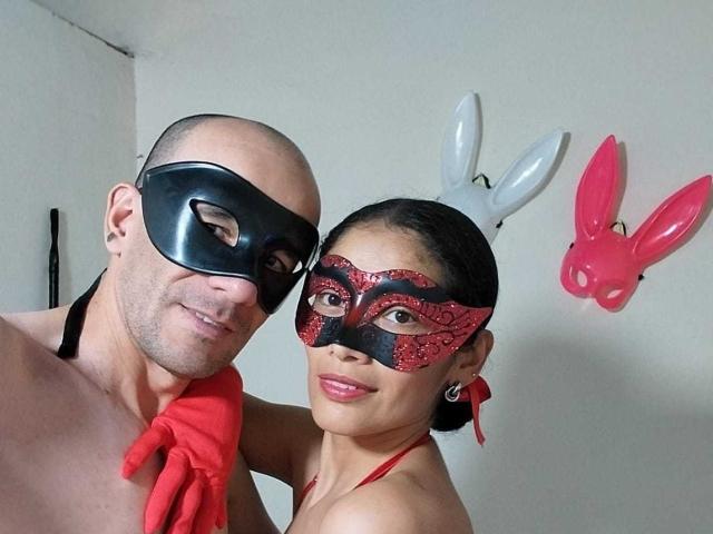 CoupleHot69s are in a selfie, wearing black and red masks, respectively. CoupleHot69s' mask has bunny ears. CoupleHot69s' mask is black, the other is red with black.