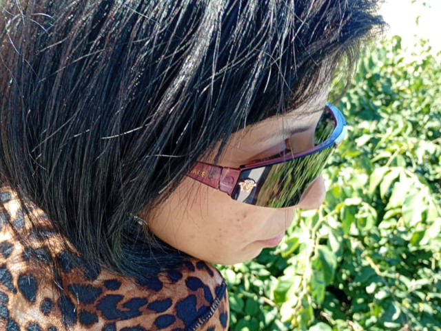 LineHt has black, straight hair with a slight shine, wearing pinkish, reflective sunglasses, and a leopard-print top. Her ass is not visible. Greenery is in the background.