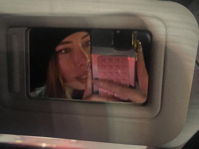 JennyLawry's reflection in a car mirror shows her holding a pink phone case with her hand, brown hair, and slightly open mouth. Her tits are partially visible.