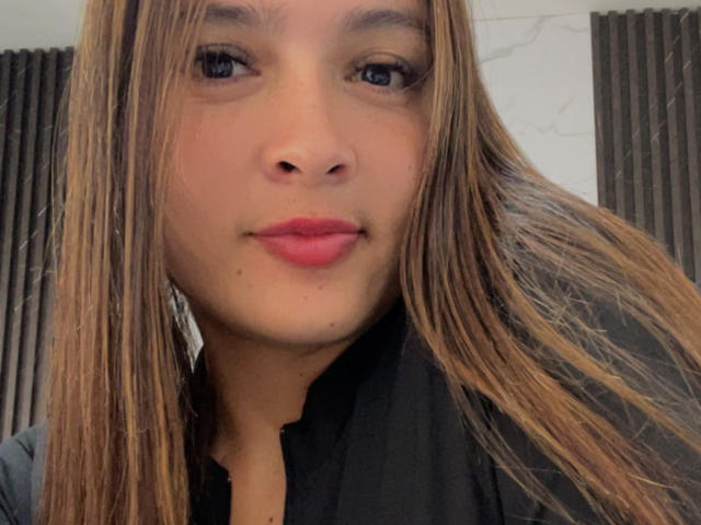 Gabrielafoxxy's face with straight brown hair, blue eyes, pink lipstick, and a small beauty mark under her right eye. She's wearing a black shirt.