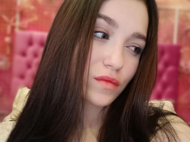 OliviaDesiree has long brown hair, pale skin, red lipstick, and a slightly wistful expression. Her small nose and subtle makeup are visible. Her tits are not shown.