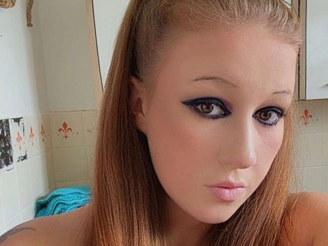 CurvyAlexaa-hot with long brown hair, blue eyeliner, and pink lips, staring at the camera with a pouty expression, showing her small nose and fair skin.