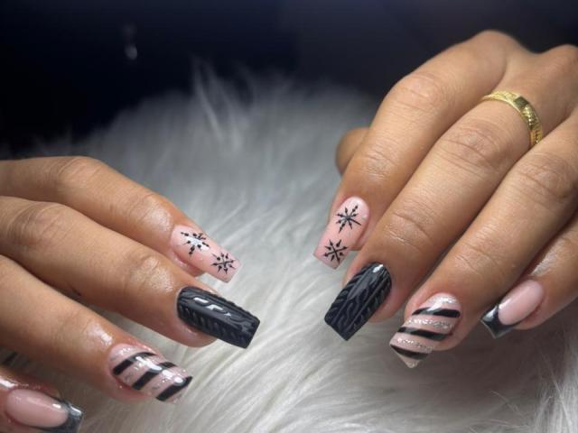 EimmyPark's nails are a dark, wintery mix with pink snowflakes, black snow patterns, and grey striped nails, resting on a fluffy white surface. She wears a gold ring.